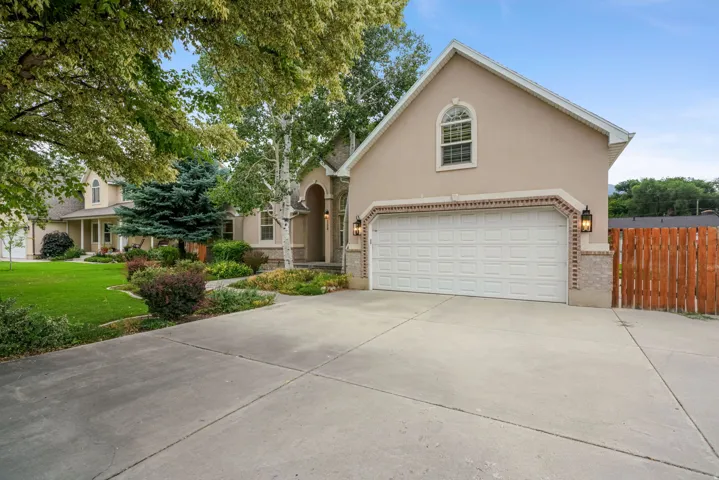 Exterior featuring a light stucco finish, a two-car garage with an arched window above, brick detailing, and a concrete driveway