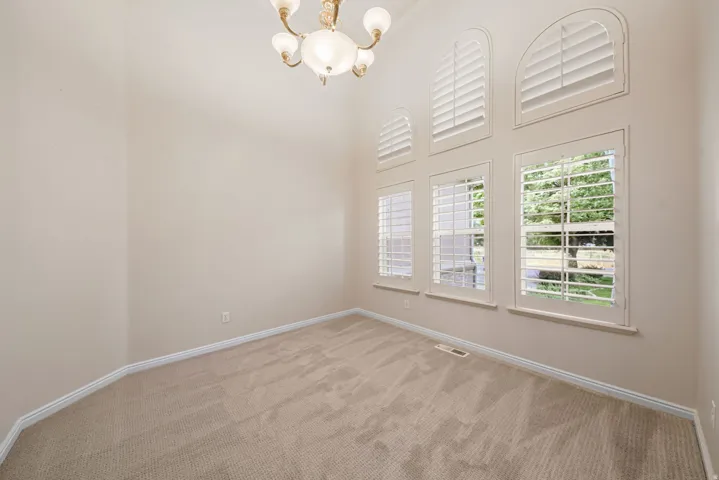 Room featuring vaulted ceilings, carpet flooring, a multi-pane window configuration with arched upper windows, white louvered plantation shutters, and an ornate ceiling-mounted light fixture