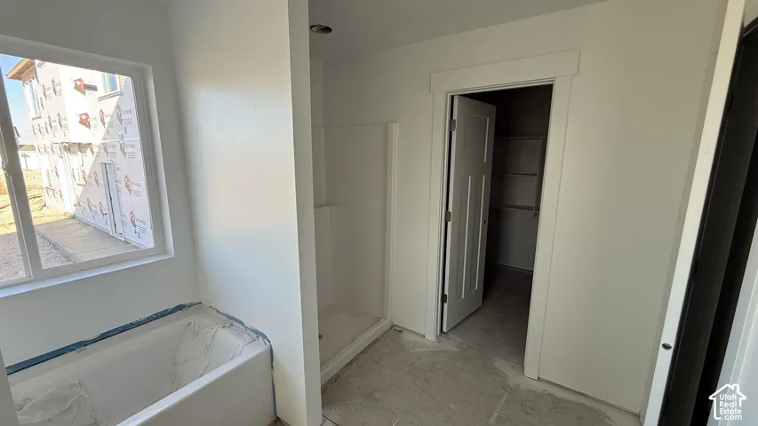 White bathtub with a window, adjacent to a standing shower stall, and a doorway with a visible closet