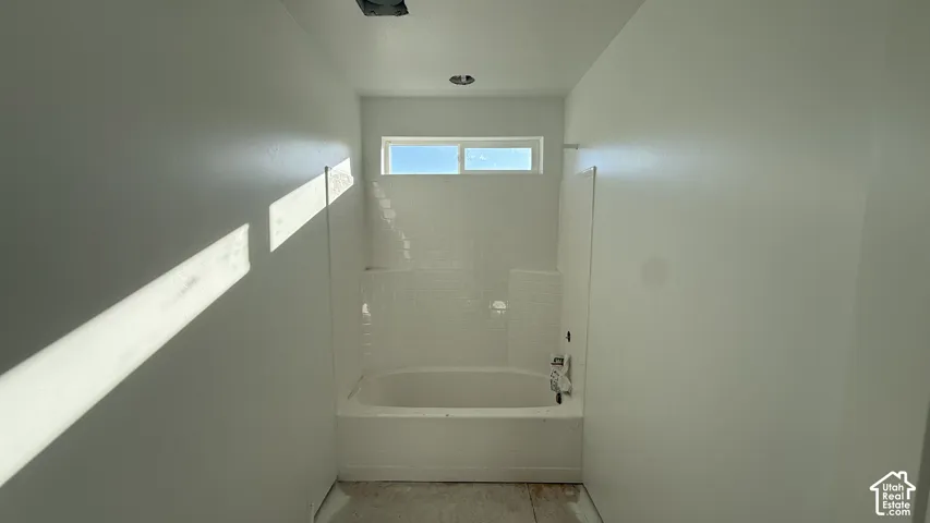 White-tiled tub with integrated shelving, chrome fixtures, and a high transom window