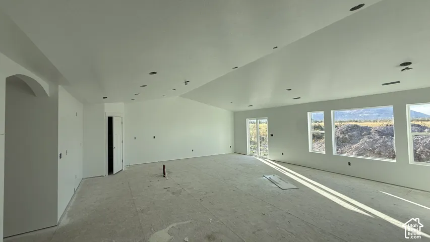 Spacious open-concept room with vaulted ceilings, recessed lighting, multiple windows, and a glass-paneled door