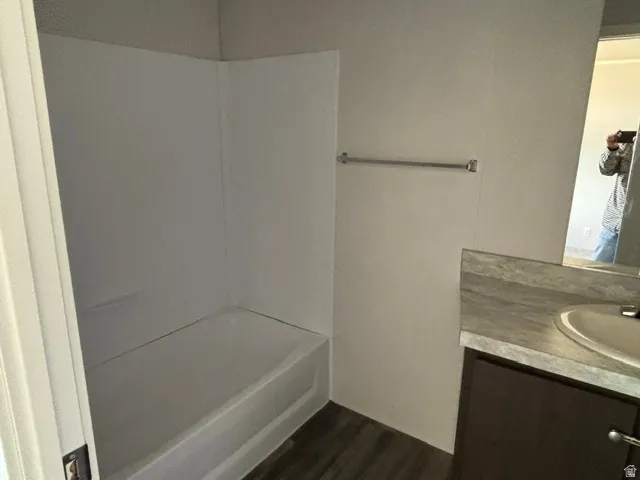 Bathroom featuring a white tub-shower combination, dark wood-finish vanity with an integrated sink, patterned countertop, and wood-finish flooring