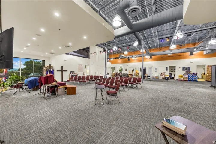 Spacious commercial interior featuring recessed lighting, exposed ductwork, large windows, and patterned carpet flooring
