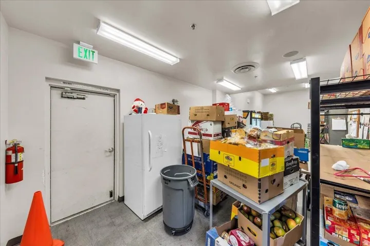 Utility space featuring a solid core door with panic bar, illuminated exit sign, and multiple fluorescent ceiling lights