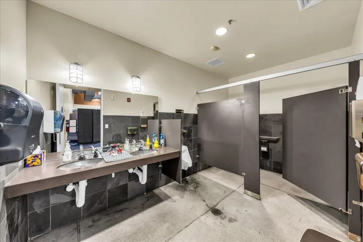 Commercial restroom featuring a dual-sink vanity with a dark countertop and wall-mounted mirrors