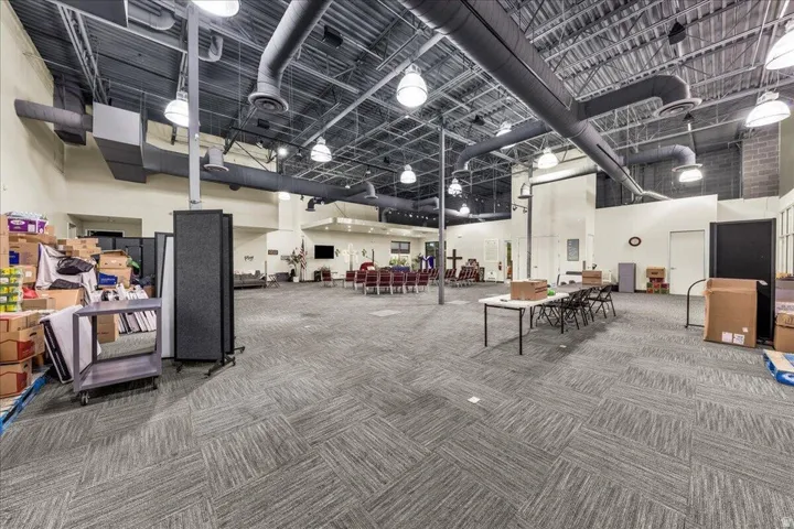 Expansive interior space featuring gray patterned carpet, exposed ductwork, and suspended industrial lighting