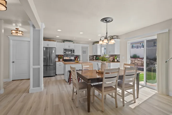 Open-concept dining area featuring wood-finish flooring, a kitchen with white cabinetry, stainless steel appliances, and a sliding glass door