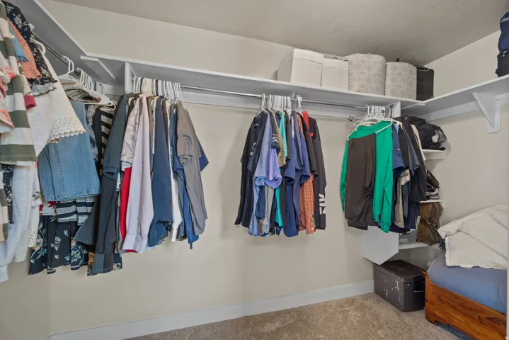 Walk-in closet featuring extensive built-in shelving, multiple hanging rods, corner shelving, and light beige wall paint