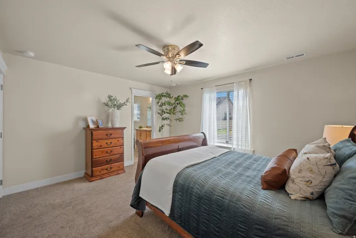 Carpeted bedroom featuring a ceiling fan with integrated lighting, neutral wall tones, and white trim