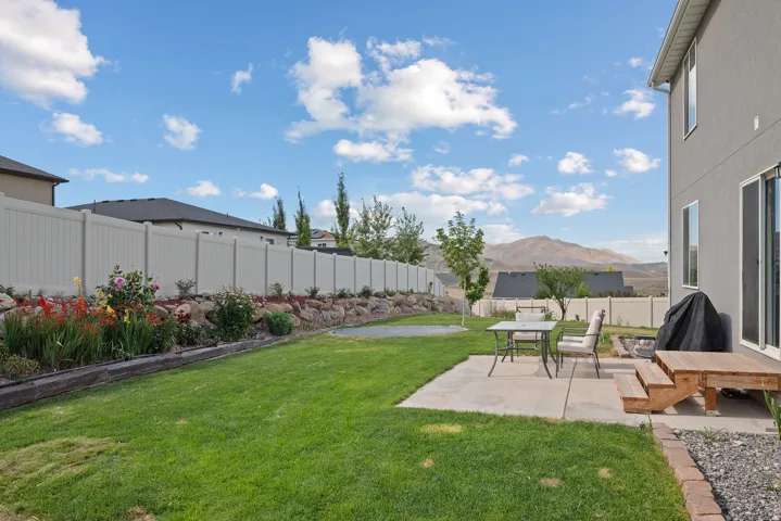 Expansive backyard featuring a lush lawn, concrete patio, and a dedicated garden bed with flowering plants and rock landscaping