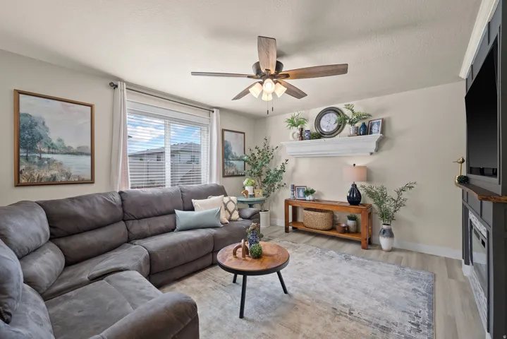 Spacious living area featuring light-toned walls, wood-finish flooring, and a ceiling fan with integrated lighting