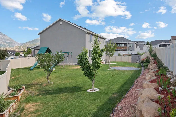 Spacious backyard featuring a sloped lawn, established trees, and a decorative rock garden with red mulch