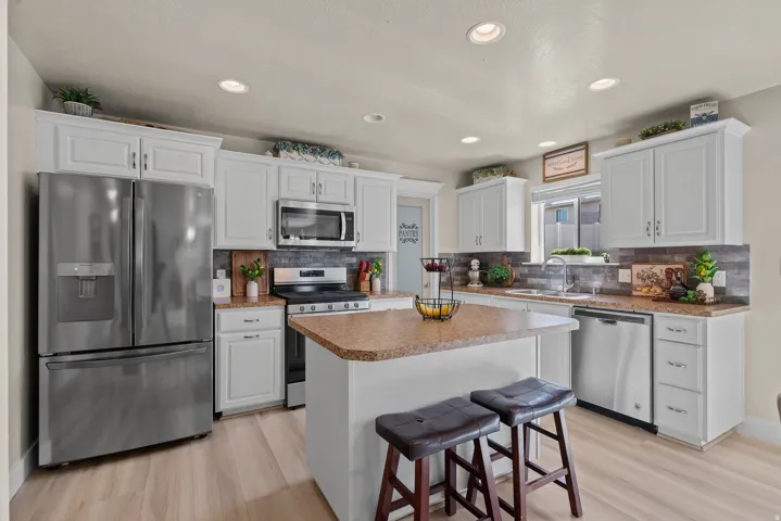 Modern kitchen featuring light wood-finish flooring, white cabinetry, stainless steel appliances, a center island with countertop seating, and recessed lighting