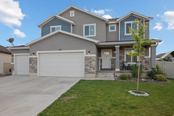 Two-story residence featuring a gray stucco and blue siding exterior with stone accents, a covered front porch, a two-car garage, and an additional single-car garage