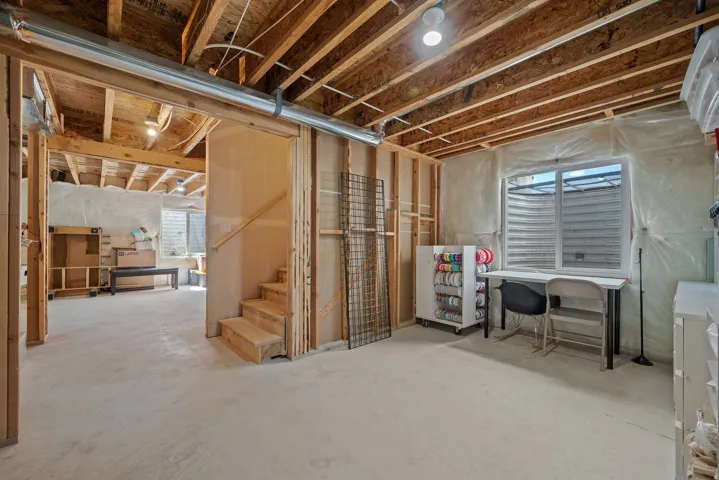 Unfinished basement with exposed wood joists and subflooring, framed wall studs, and a concrete floor