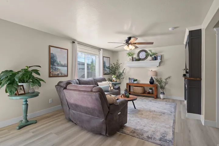 Spacious living area featuring light-toned walls, wood-finish flooring, and a ceiling fan with integrated lighting
