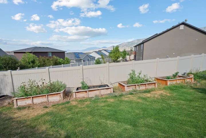Spacious backyard featuring a manicured lawn, multiple raised garden beds, and a perimeter privacy fence