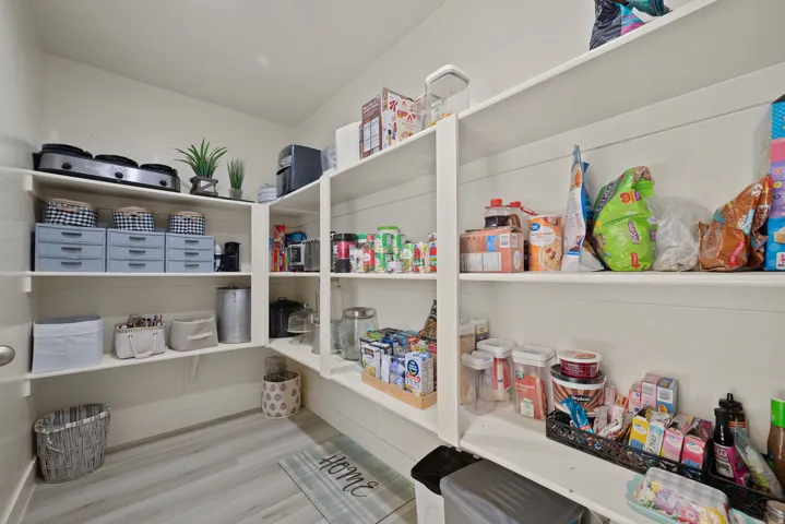 Spacious walk-in pantry featuring white shelving, shiplap wall accents, and wood-finish flooring