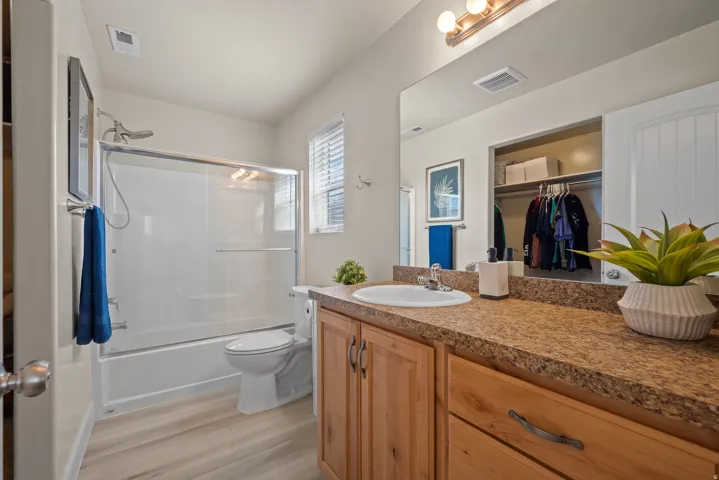 Bathroom featuring a light wood-finish vanity with a speckled countertop, an integrated sink, and a wall-mounted mirror