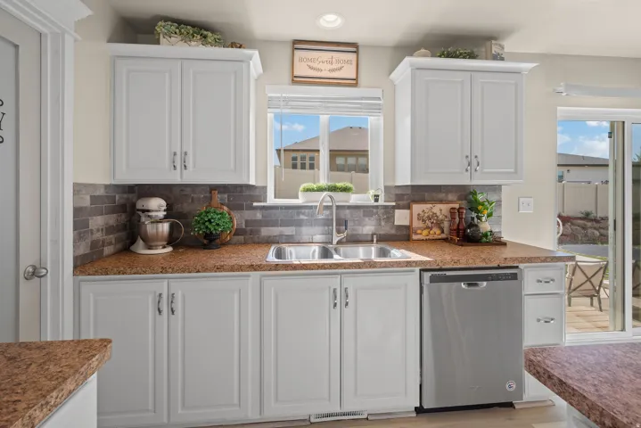 Kitchen featuring white cabinetry, stone-look countertops, a tile backsplash, and a stainless steel double sink