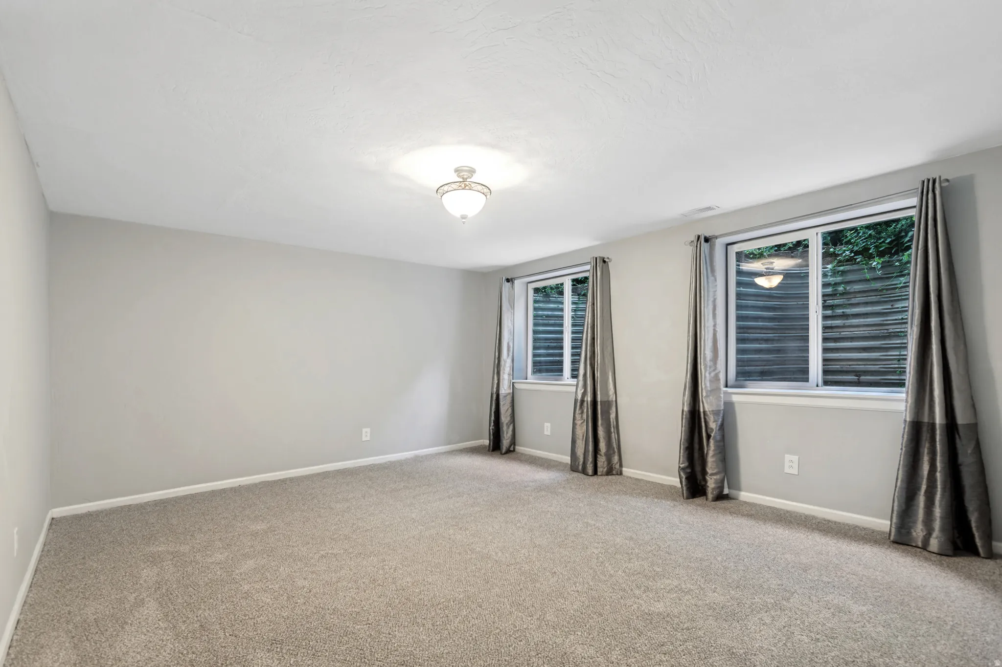 Spacious room featuring light gray walls, plush carpeting, and two egress windows