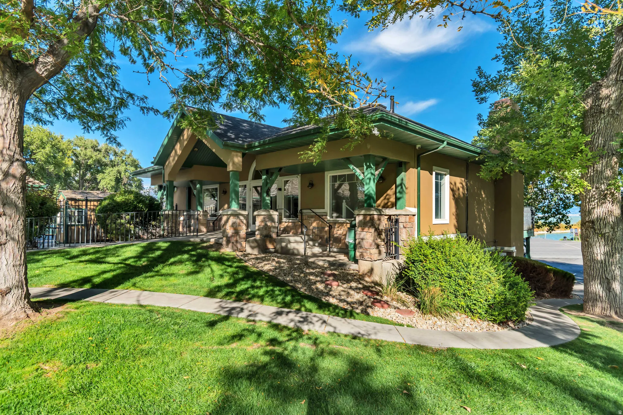 Exterior featuring a covered porch with stone-clad pillars, a dark roof, and a light-colored stucco finish