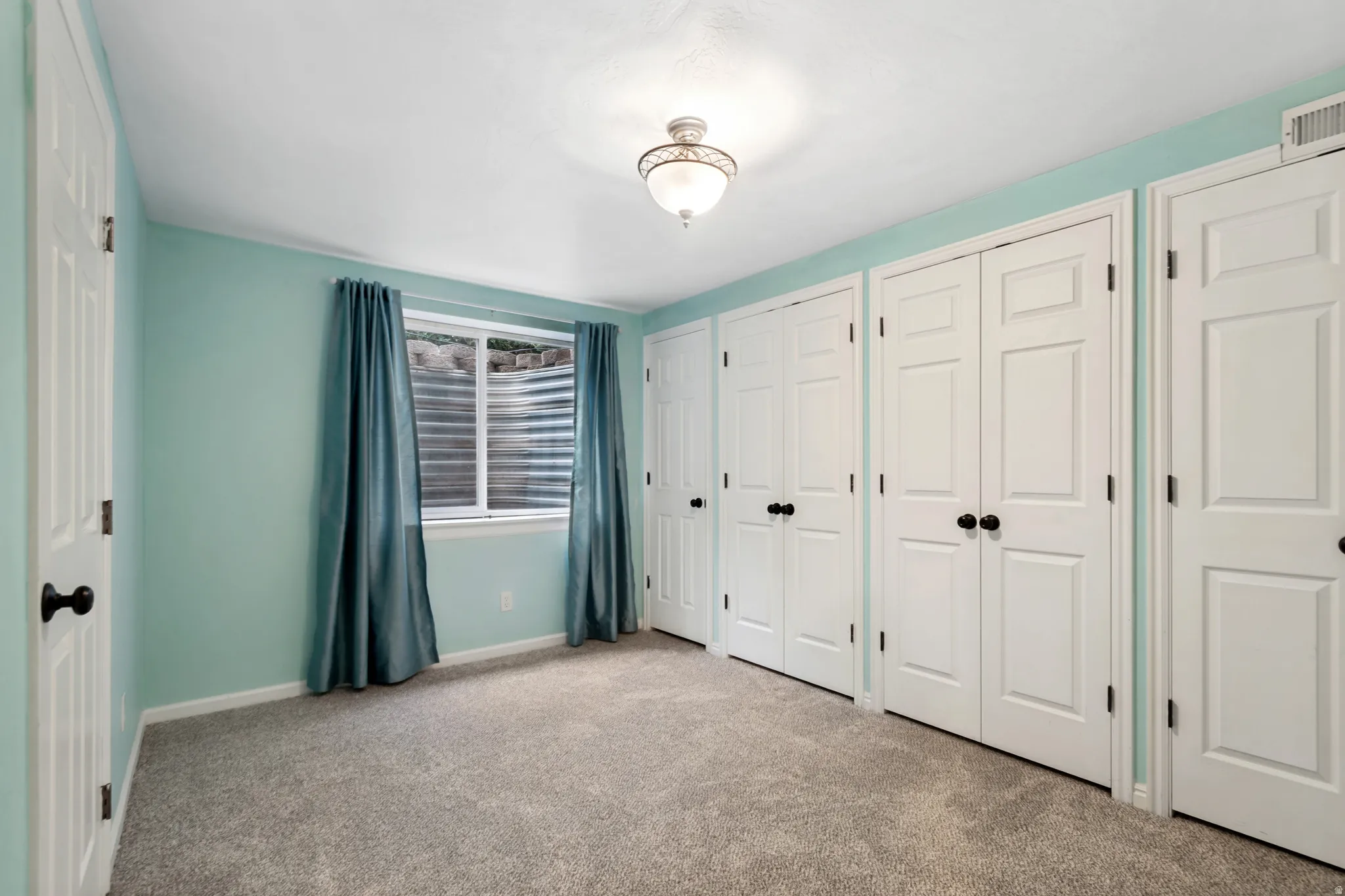 Bedroom featuring light blue walls, gray carpet flooring, a window with horizontal blinds, and multiple white paneled doors
