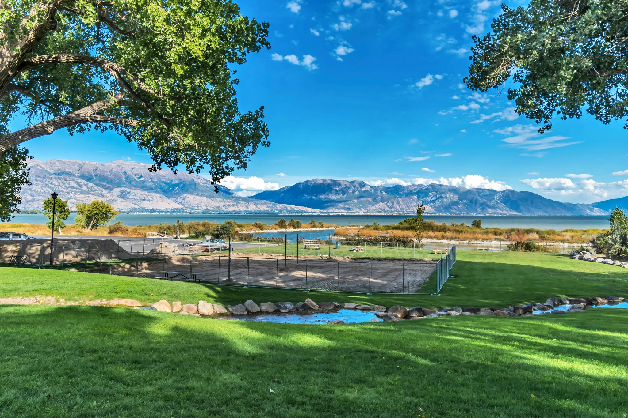 Expansive green lawn with a winding stream and natural rock accents, framed by mature trees