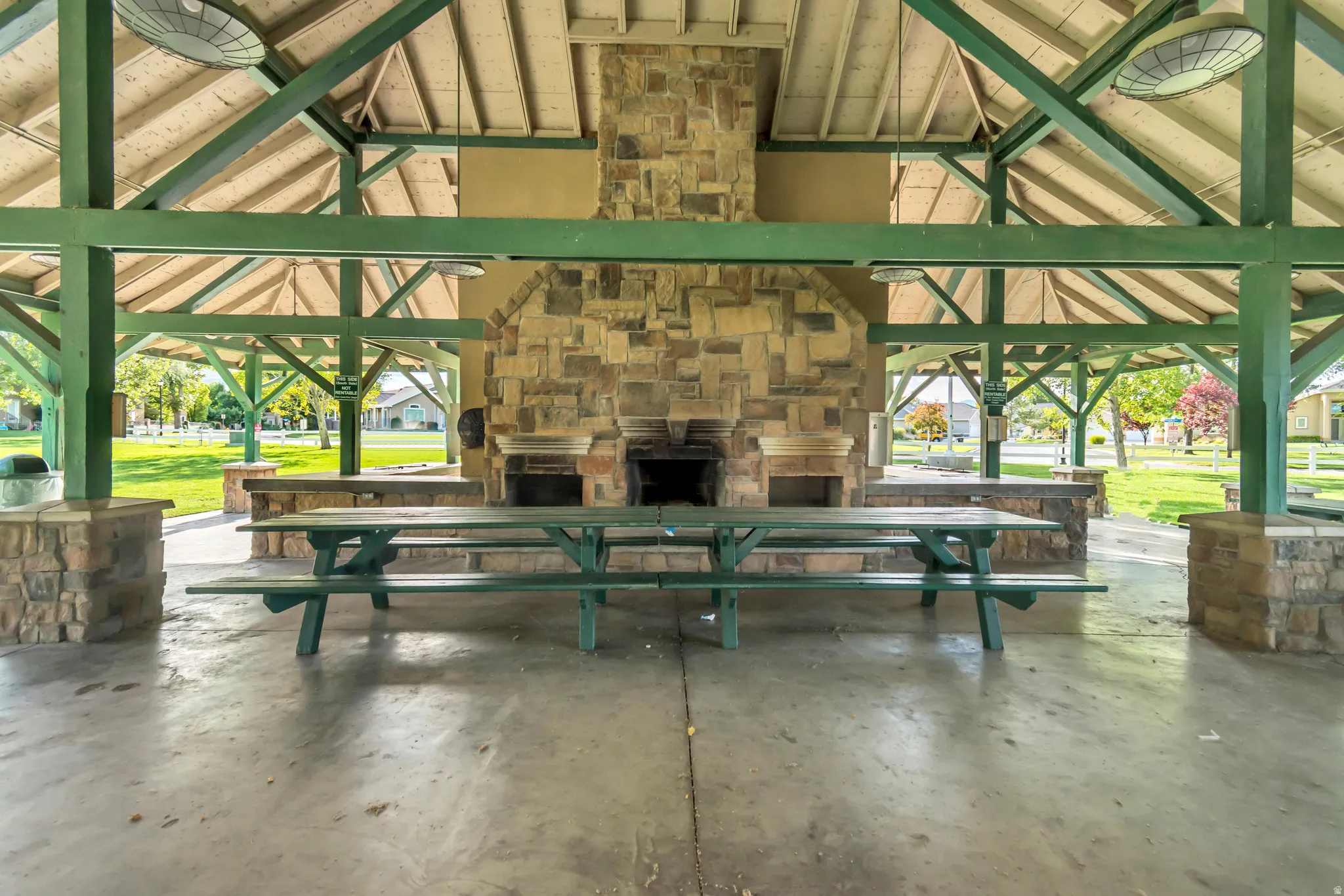 Expansive covered pavilion featuring exposed beam construction, a stone-clad fireplace and barbecue area, integrated stone-finish countertops, and a concrete floor
