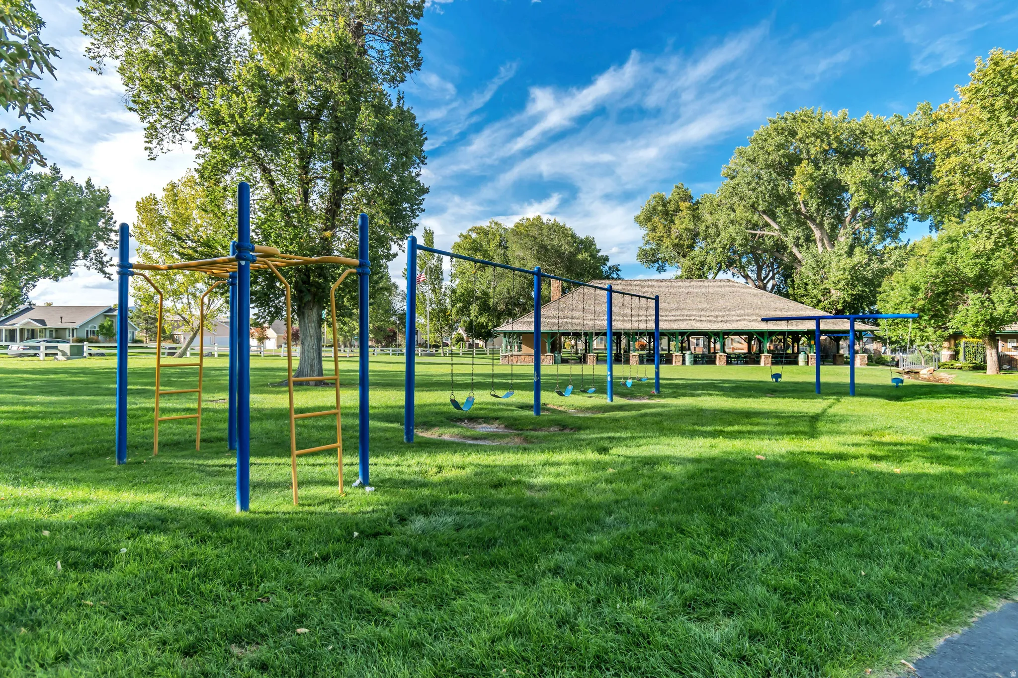 Community park with vibrant blue and yellow playground equipment, large swing sets, and expansive green lawns