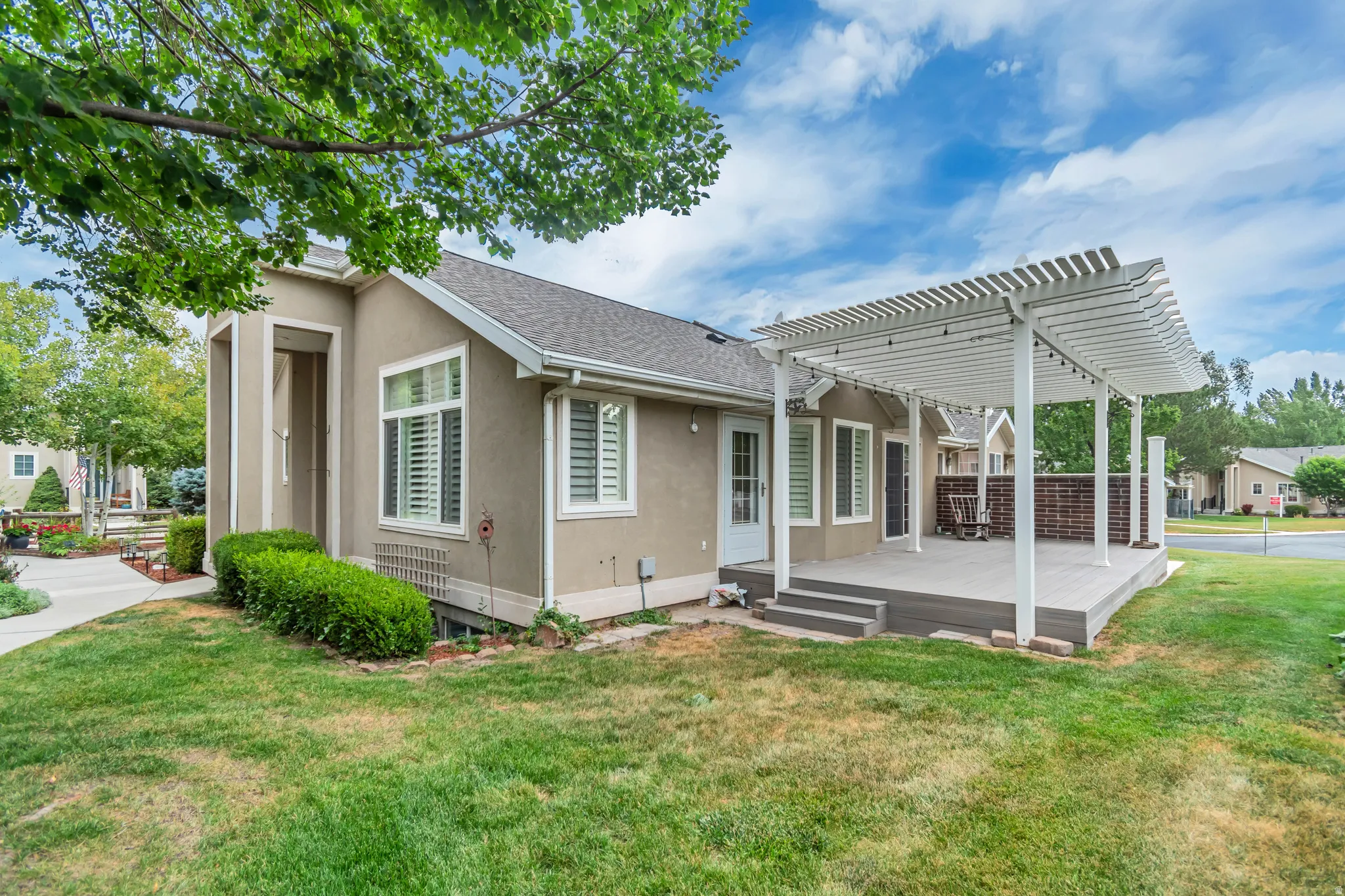 Rear exterior featuring a multi-level composite deck with a white pergola, brick accent wall, and multiple entry points