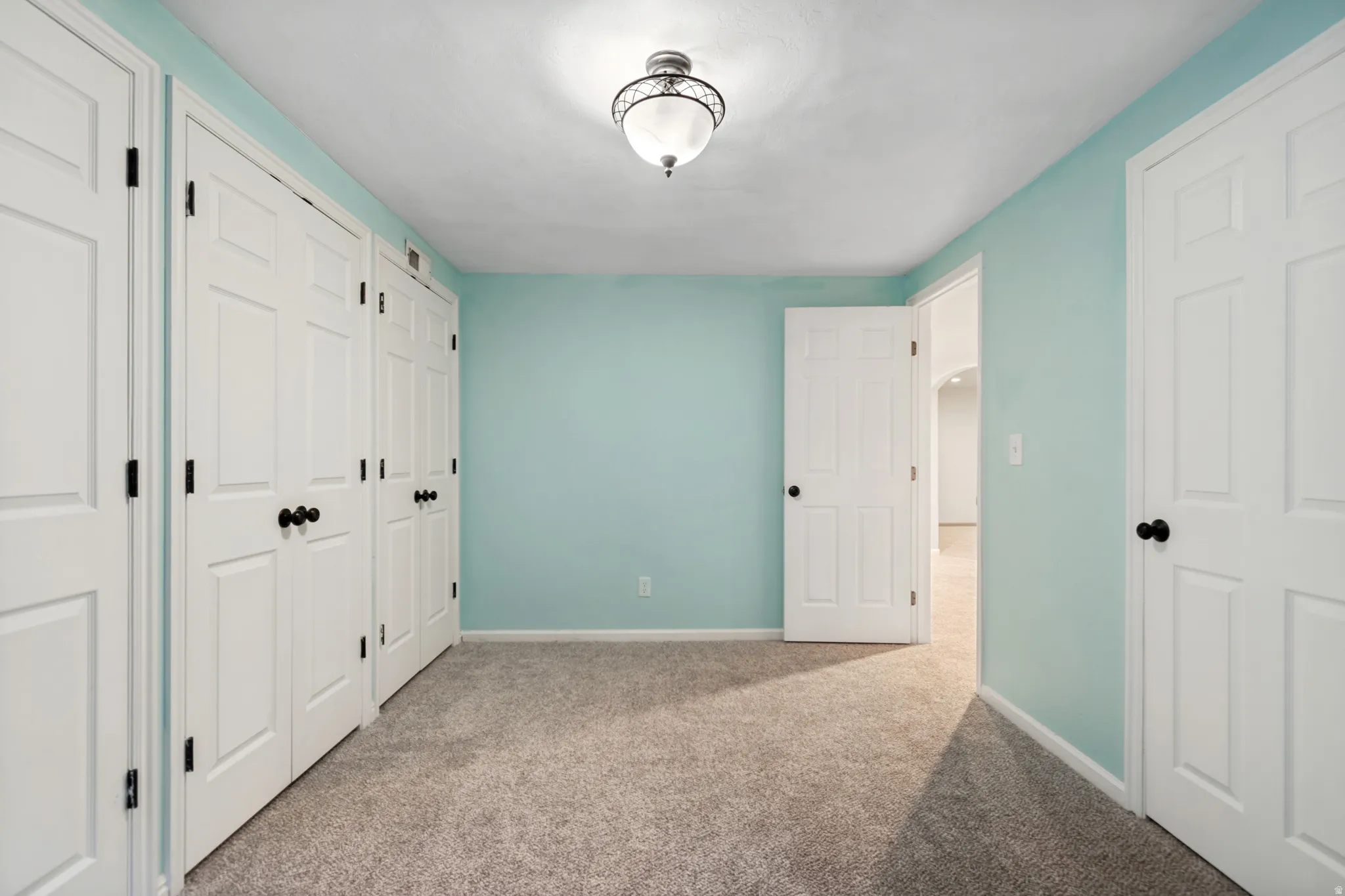 Room featuring light blue wall paint, gray carpet flooring, white trim, white paneled doors with black hardware, and an overhead semi-flush mount light fixture