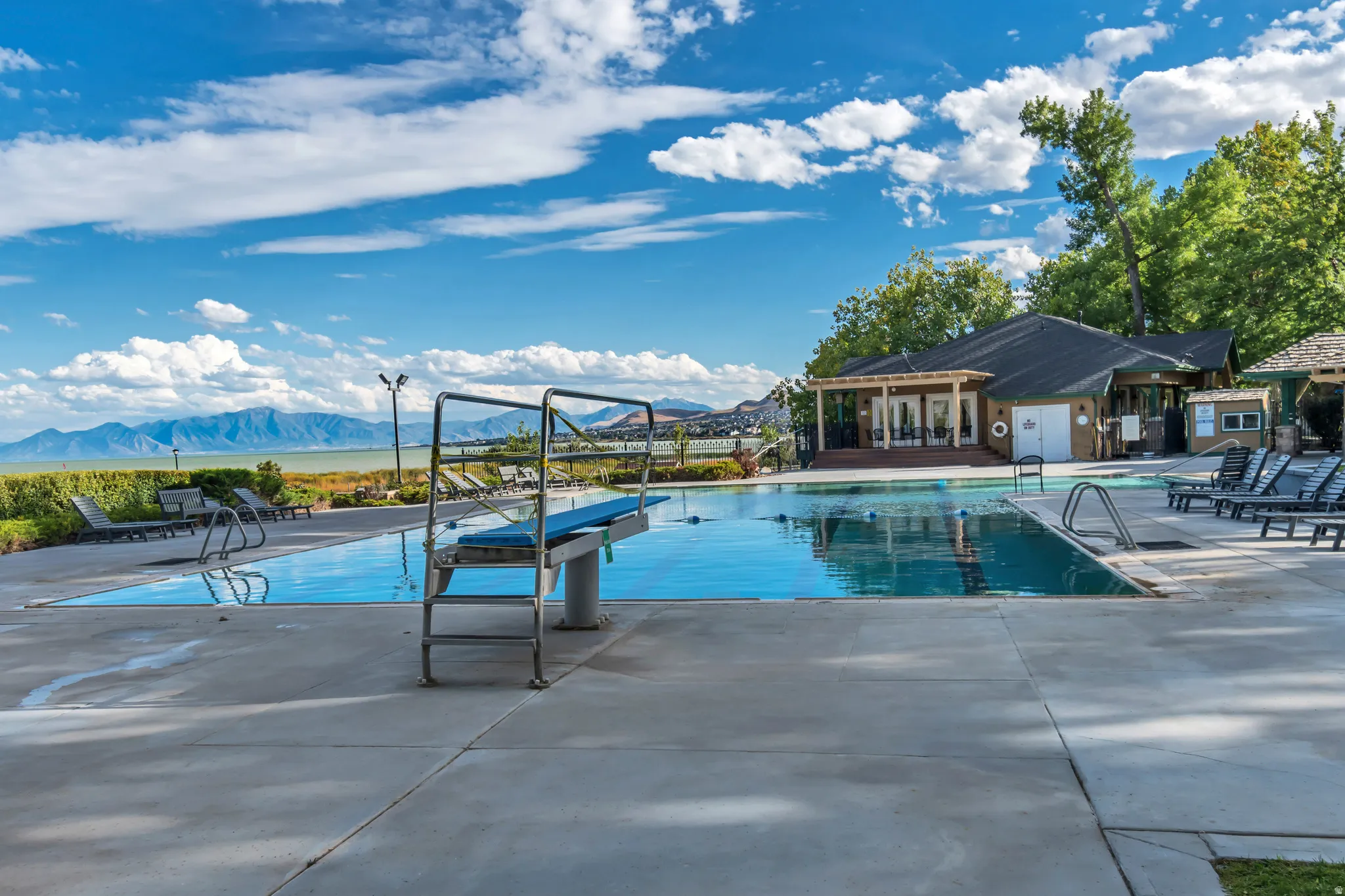 Outdoor swimming pool featuring a diving board, surrounding concrete patio, and lounge chairs
