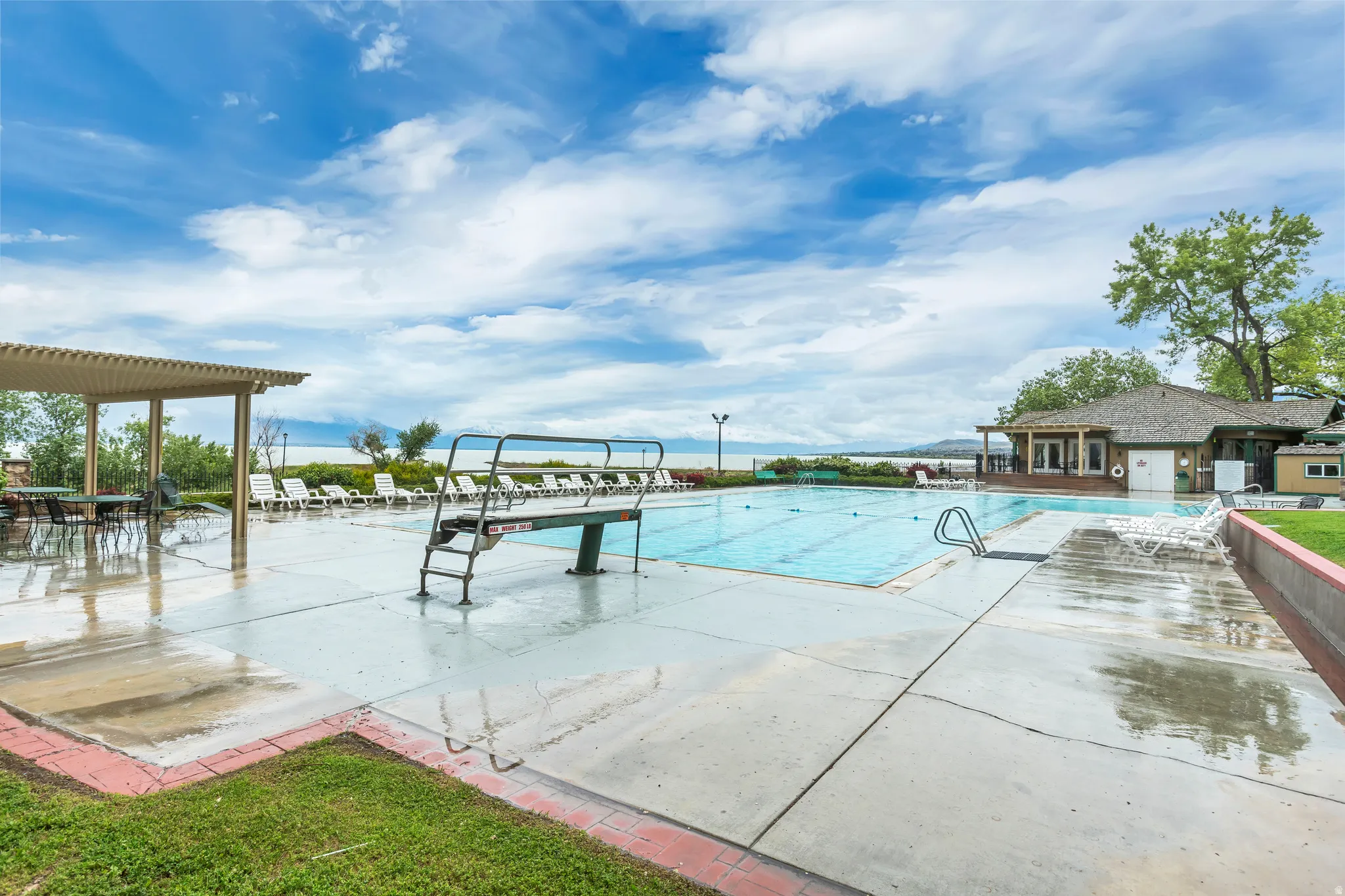 Expansive outdoor swimming pool with a diving board and entry steps, surrounded by concrete decking