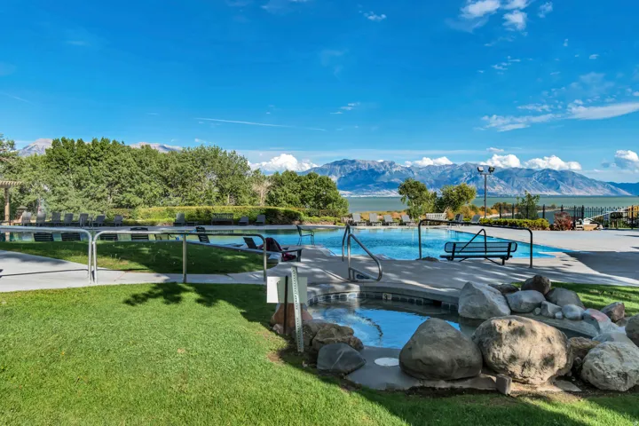 Resort-style pool area featuring a large swimming pool, integrated hot tub with rock surround, ample lounge seating, and manicured lawns