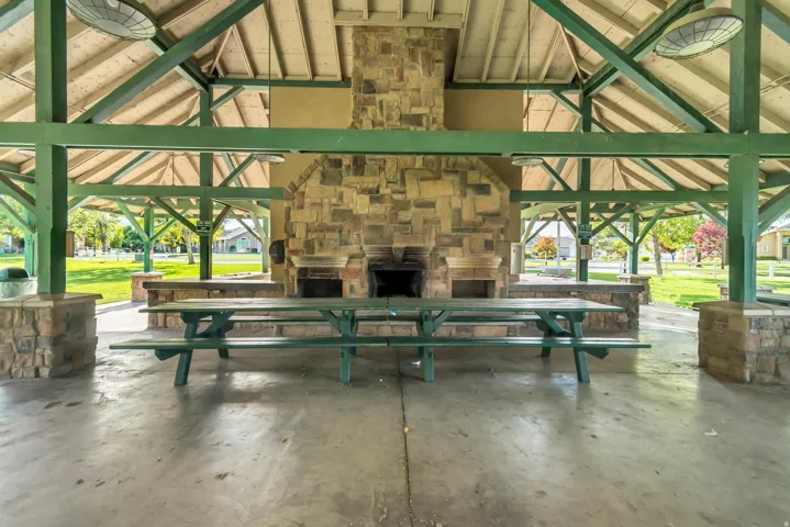 Expansive covered pavilion featuring exposed beam construction, a stone-clad fireplace and barbecue area, integrated stone-finish countertops, and a concrete floor