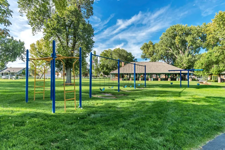 Community park with vibrant blue and yellow playground equipment, large swing sets, and expansive green lawns