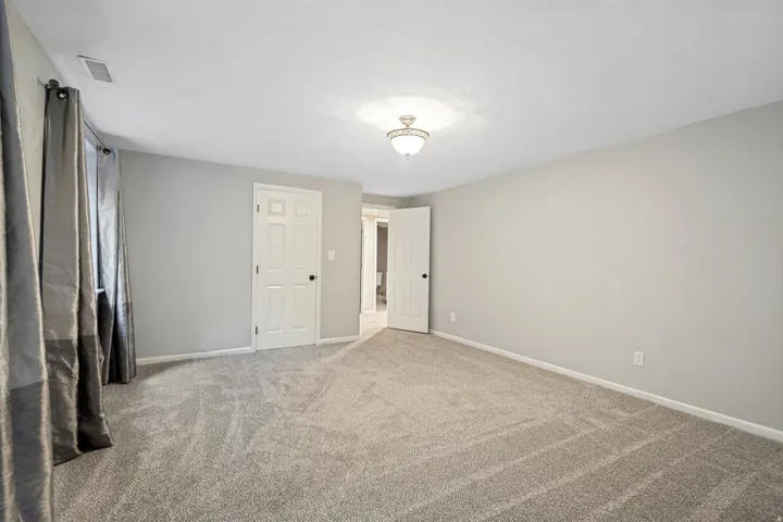 Spacious room featuring neutral carpeting, light gray walls, a white paneled door, and a semi-flush mount ceiling fixture