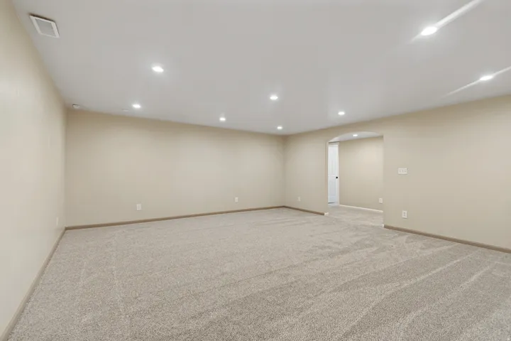 Spacious room featuring neutral carpeting, light beige wall paint, recessed ceiling lighting, and a wide arched entryway