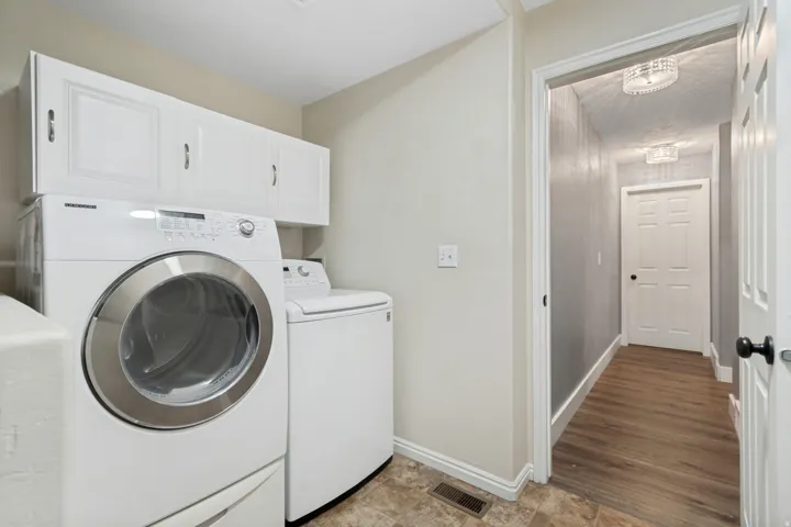 Dedicated laundry area featuring white shaker-style cabinetry, a front-loading washer, and a top-loading dryer