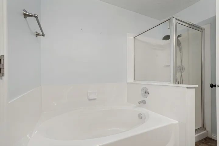 White soaking tub featuring chrome fixtures and a separate glass-enclosed shower