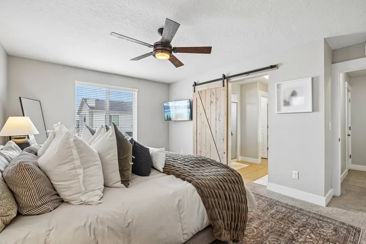 Bedroom featuring a contemporary ceiling fan, window with blinds, light gray walls, and a barn door