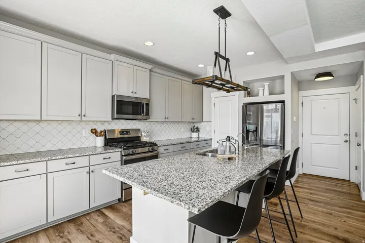 Modern kitchen featuring gray shaker cabinetry, stainless steel appliances, speckled stone countertops, and a white arabesque tile backsplash