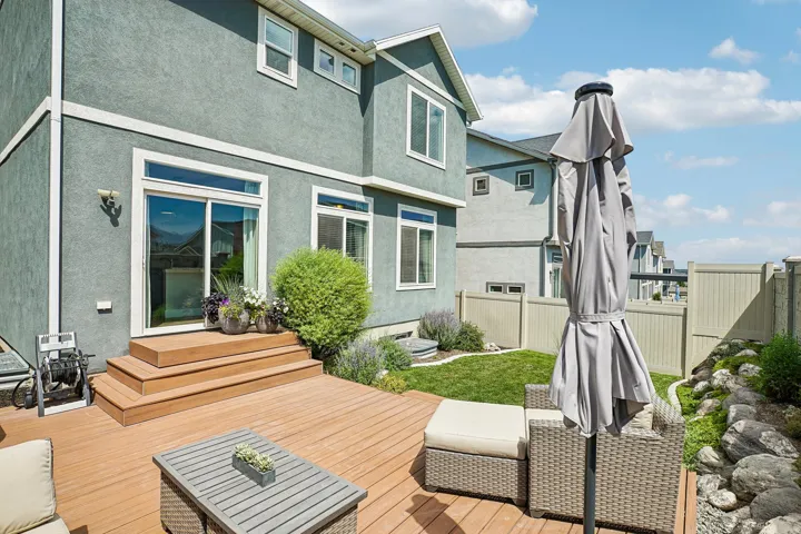 Rear exterior featuring a spacious wood-finish deck with integrated steps, a sliding glass door, and multiple windows
