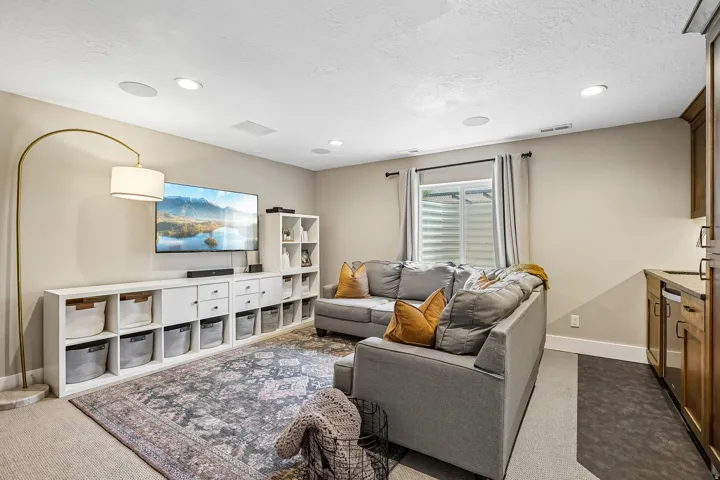 Spacious living area featuring recessed lighting, a built-in media console with storage, a large area rug, and a wet bar with wood-finish cabinetry and an integrated beverage cooler
