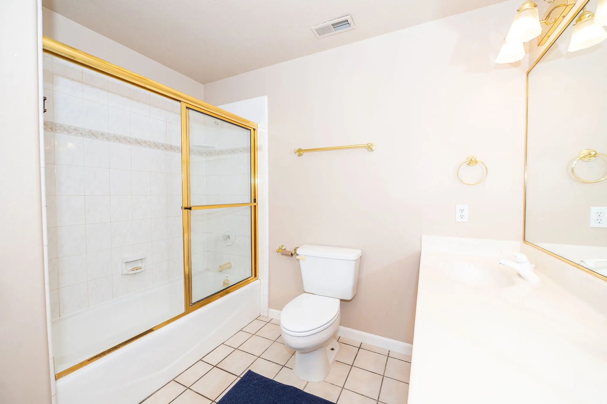 Full bathroom featuring a white tub with gold-framed sliding glass doors, white subway tile surround, white toilet, and a vanity with an integrated sink
