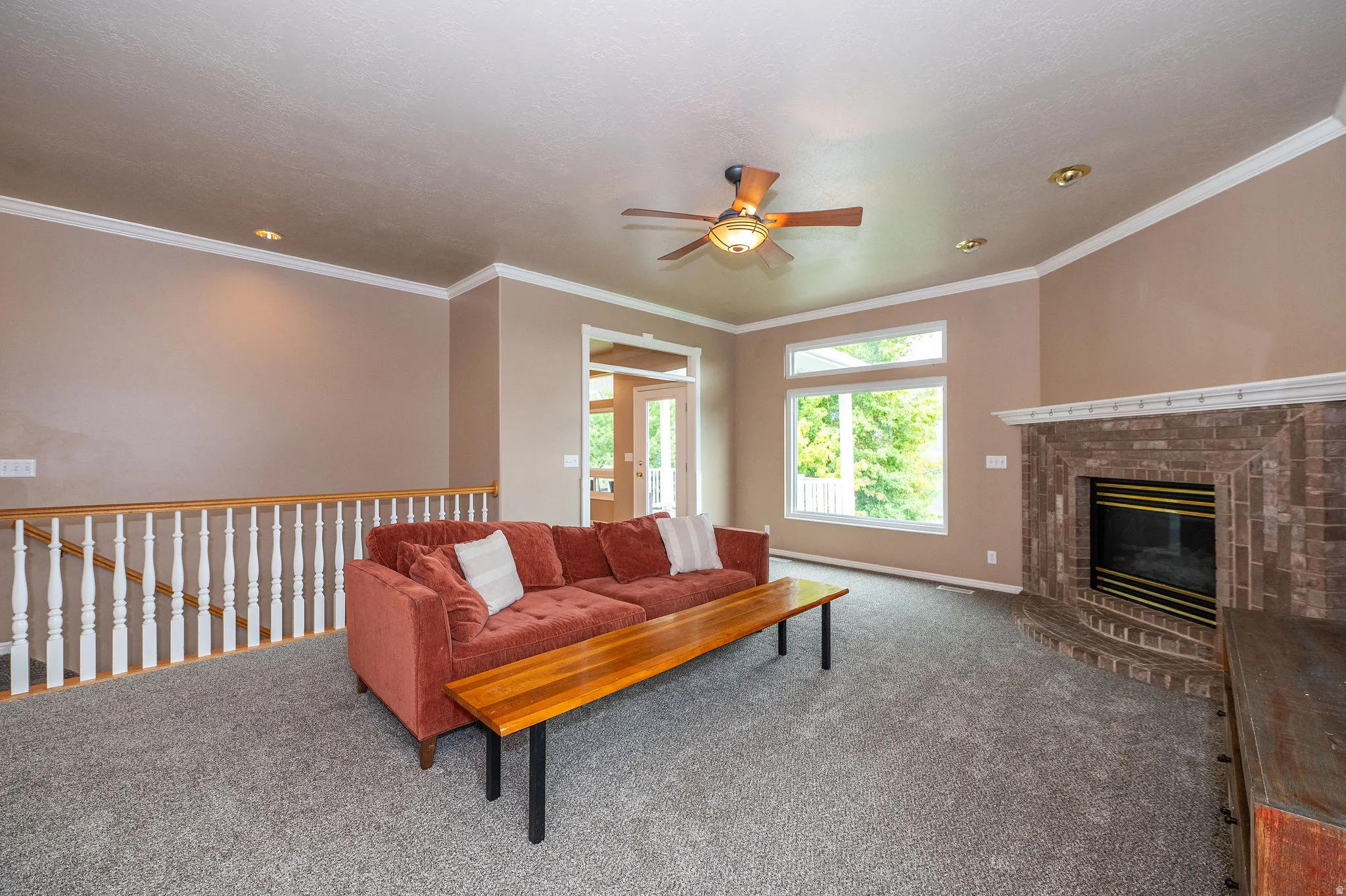 Living area featuring a brick fireplace, grey carpet, ceiling fan, and large windows