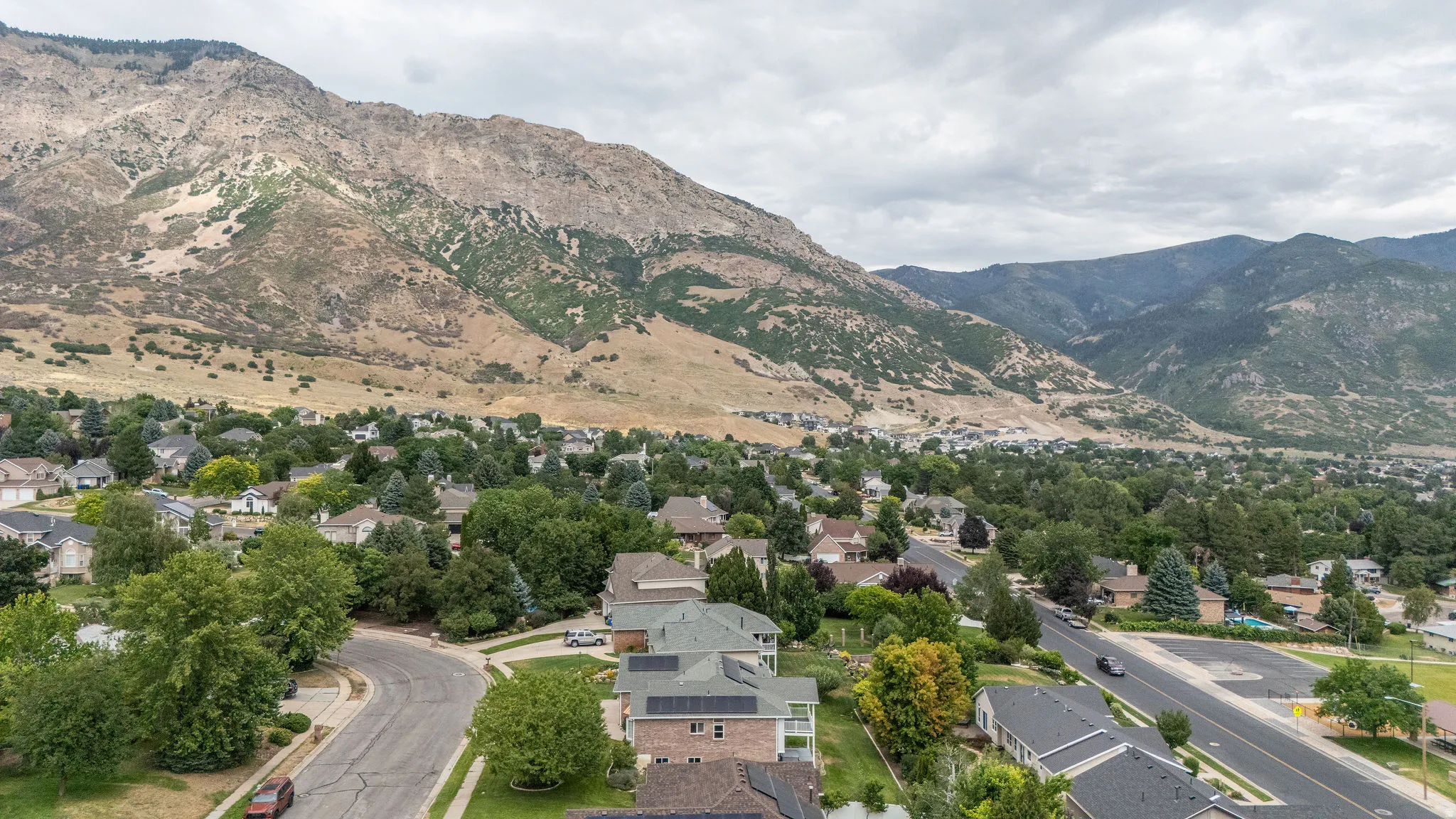 Residential neighborhood situated at the base of expansive mountains, featuring mature trees and established homes