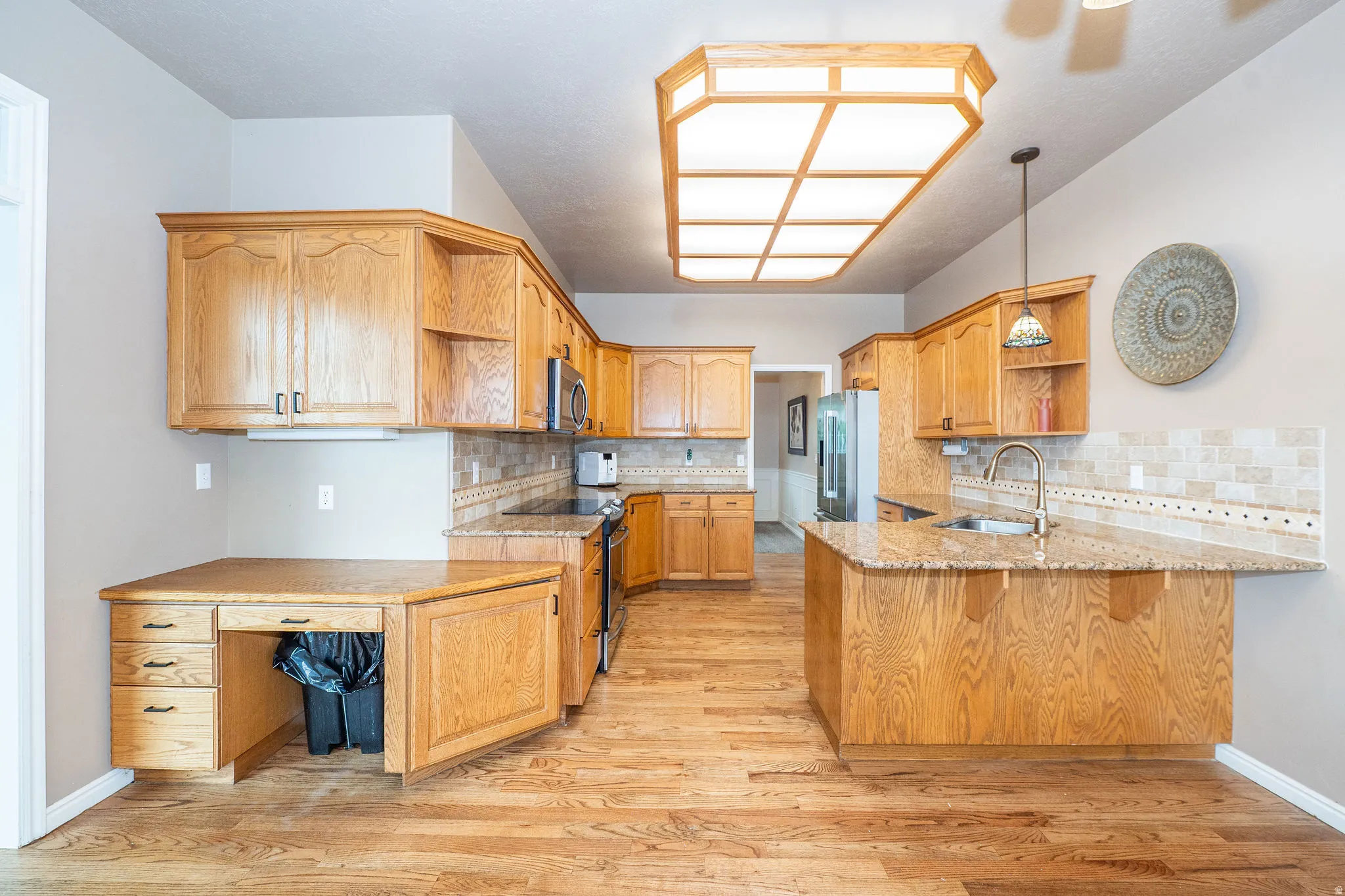 Kitchen featuring wood-finish flooring, a full suite of stainless steel appliances, light-toned cabinetry, light-toned countertops, and a tiled backsplash