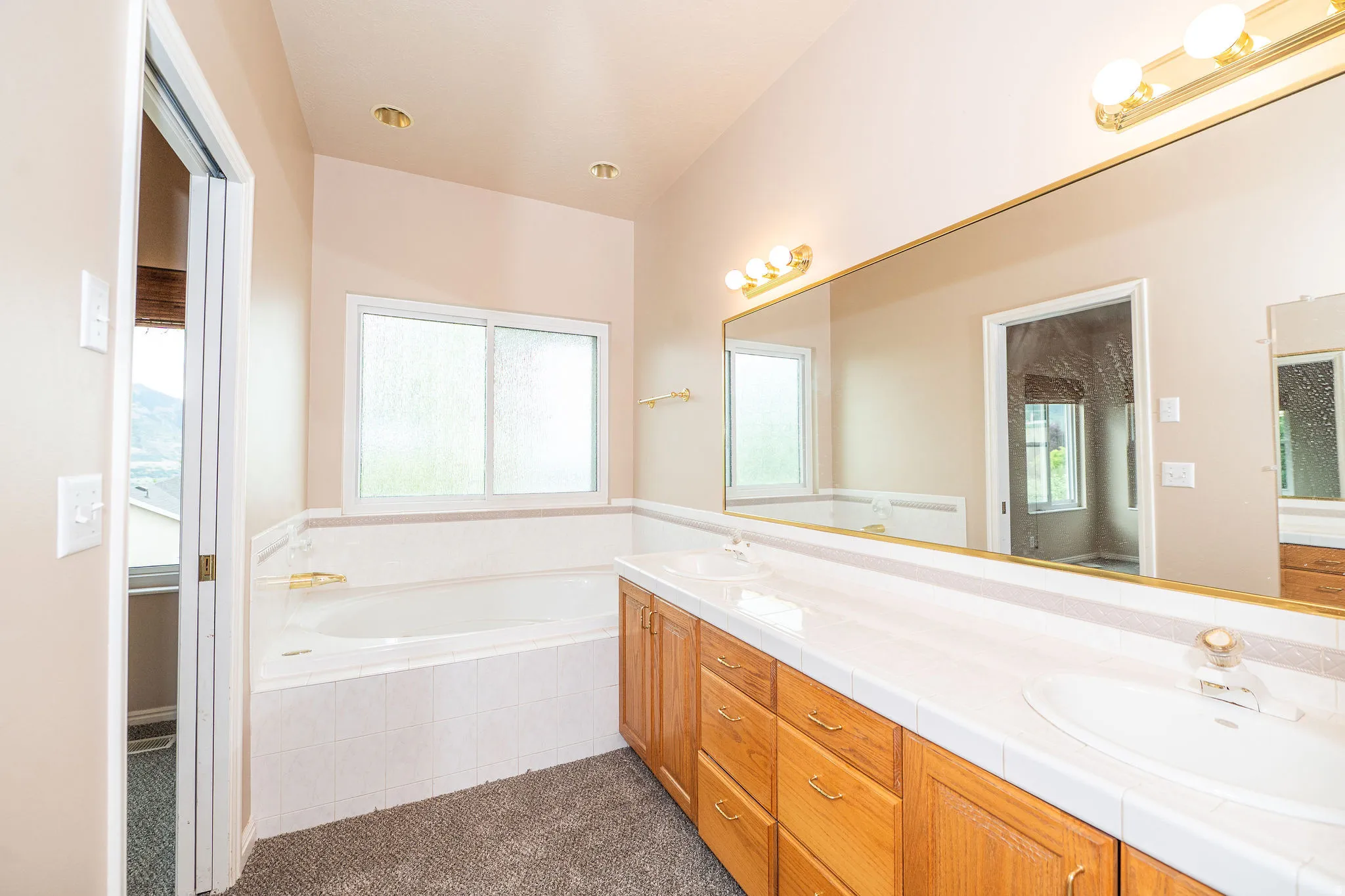 Bathroom featuring a built-in soaking tub, dual vanity with integrated sinks, wood-finish cabinetry, and a large wall-mounted mirror